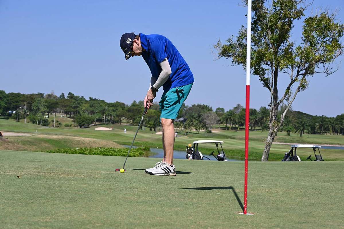 A golfer lines up a putt on a sunny green concentrating as the ball rolls toward the hole