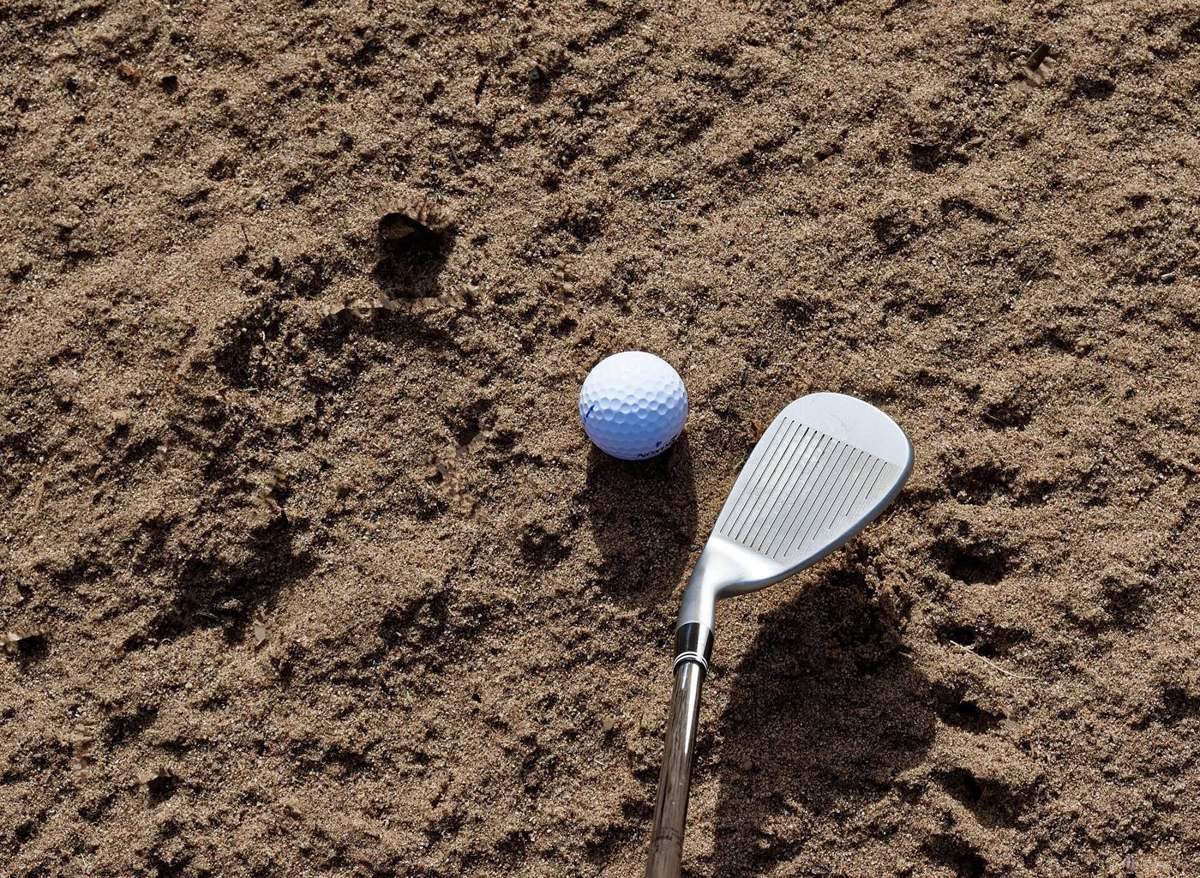A sand wedge next to a golf ball in a bunker
